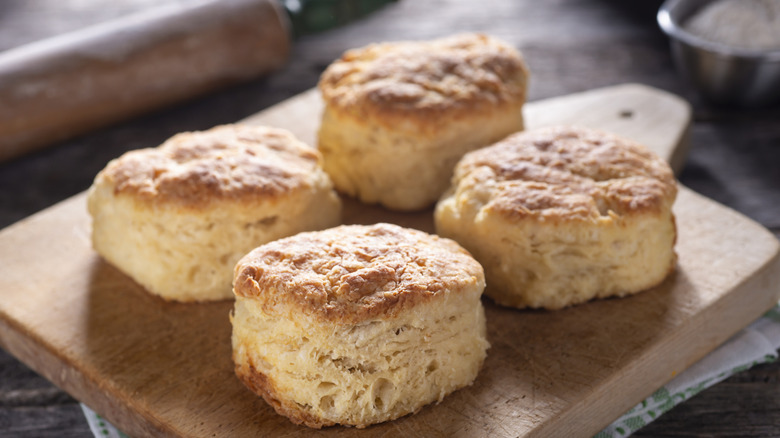 A wooden cutting board holding four perfectly golden Southern-style buttermilk biscuits