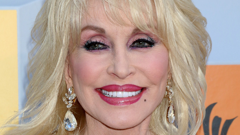 Dolly Parton smiles with pink lipstick and diamond earrings