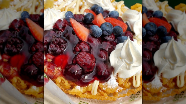 A plate of funnel cake topped with gooey pie filling, whipped cream, and fresh strawberries, blueberries, and blackberries.