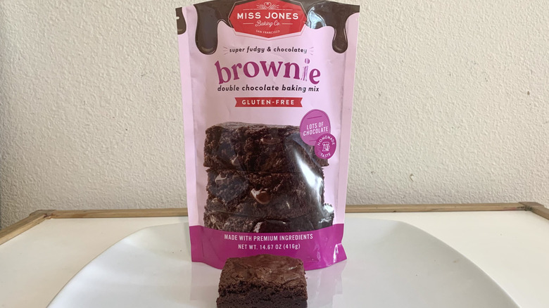 A bag of  Miss Jones Gluten-Free Double Chocolate Brownie Mix behind a baked brownie