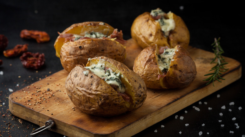four baked potatoes with cheese on wooden board