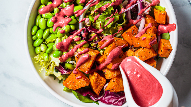 Salad of sweet potatoes, edamame, and greens with pink beet dressing drizzled over top