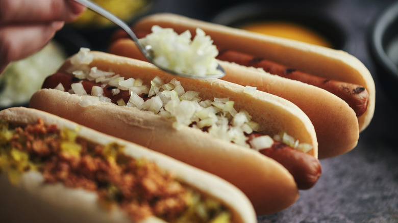 A trio of hot dogs and someone is putting onions on the middle one.
