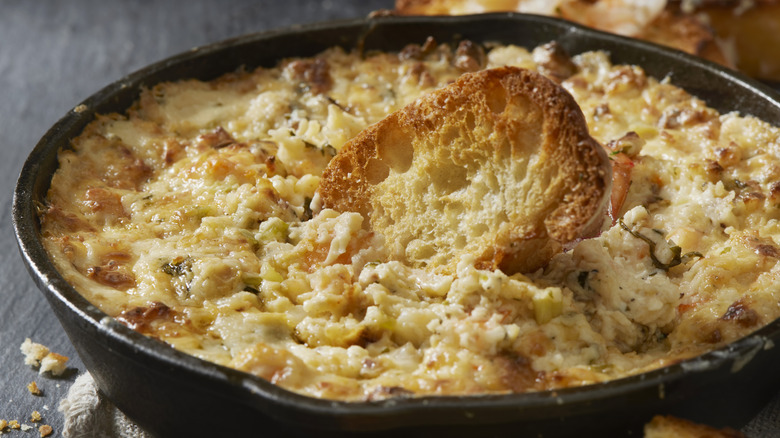 baked shrimp dip, shown in a cast iron frying pan with toated crostini, on a dark gray countertop