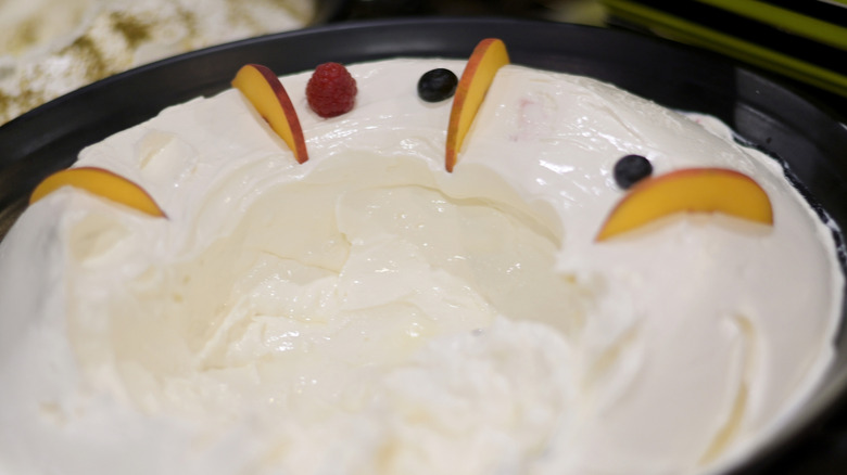 creamy dip for fruit, served in a dark bowl and garnished with fresh berries and thin slices of peach