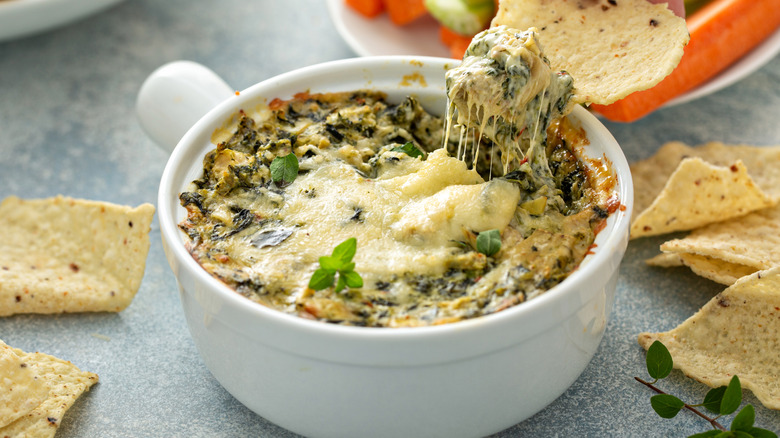 a small baking dish of hot dip, with a tortilla chip scooping out a mouthful of dip