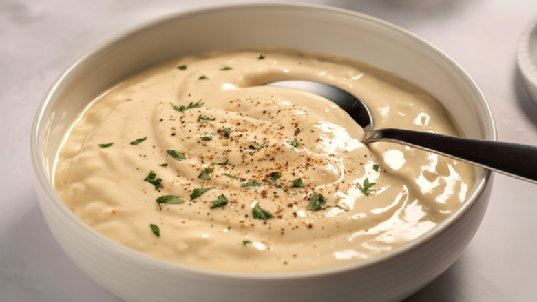 spoon resting in a white bowl filled with creamy dip, which is topped with herbs and spices, and appears to have finely diced vegetables in the body of the dip