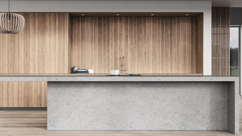 A concrete kitchen island in a room paneled with wood
