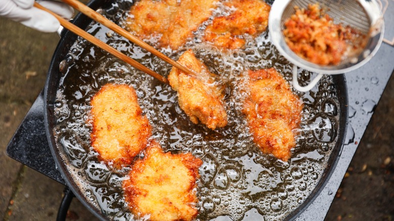Pieces of chicken frying in oil being turned with chopsticks