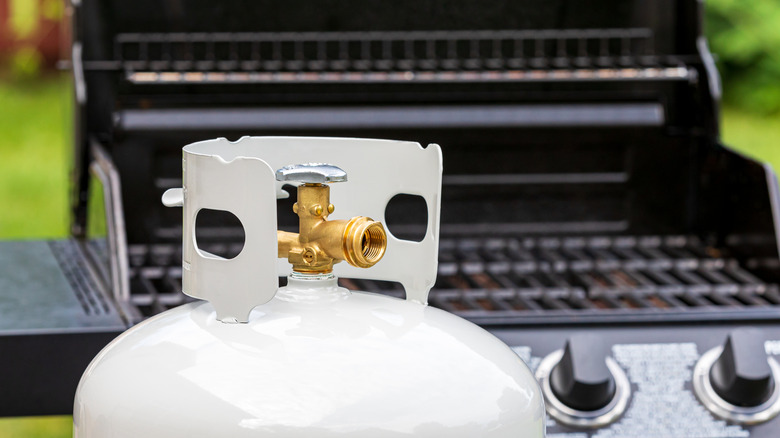 White propane tank in front of gas grill
