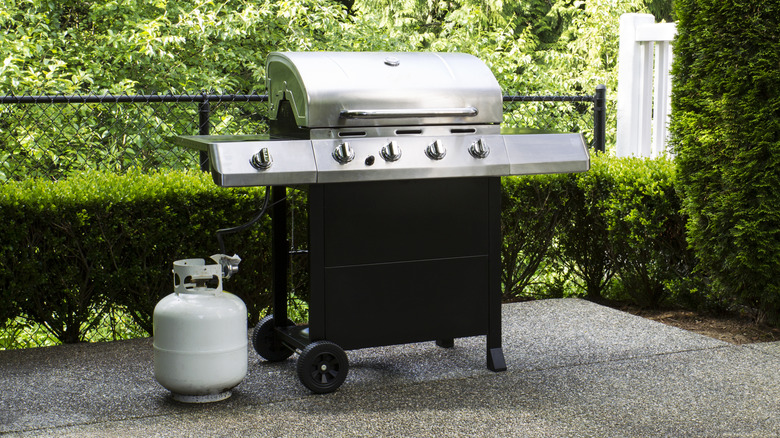 Steel outdoor grill with white propane tank beside it