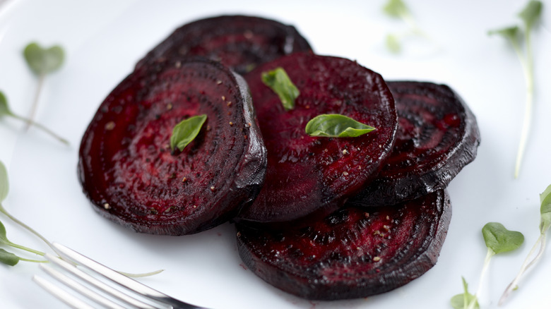 Caramelized roasted beet slices on white plate with herb garnish and silver fork