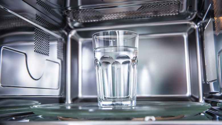 A glass of water inside of a shiny microwave