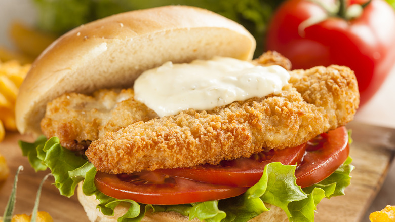 A breaded fish sandwich on a bun with lettuce, tomato, and tartar sauce