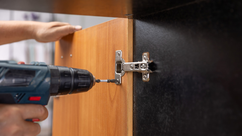 A person securing a hinge with a drill