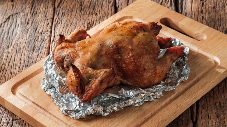 Whole roasted chicken in crumpled foil on a cutting board