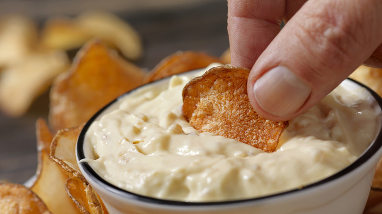 hand dipping potato chips into sour cream dip