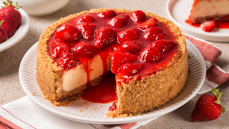 homemade deep dish strawberry cheesecake with half strawberries and sauce on top and a graham cracker crust.