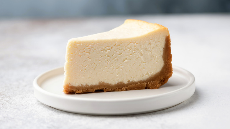slice of homemade classic New York cheesecake on a white plate against a light background.