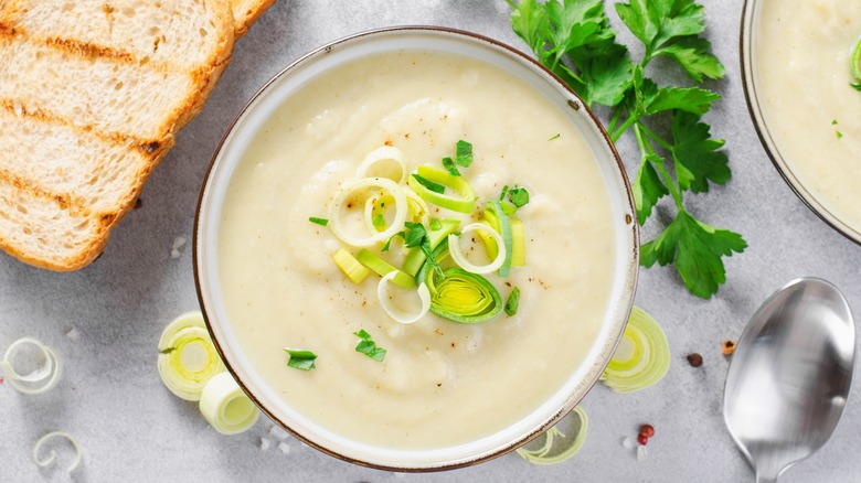 Potato leek soup with parsley garnish beside bowl