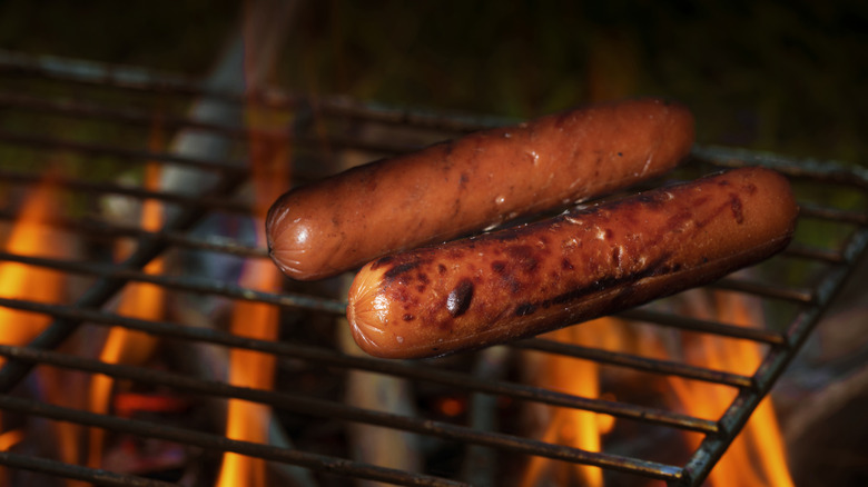 Two hot dogs on a grill grate above flames