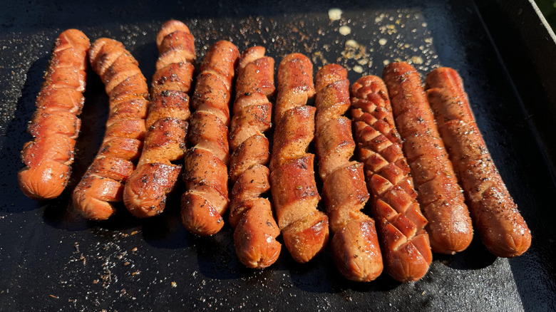 Hot dogs sliced in a variety of different ways cooking on a griddle
