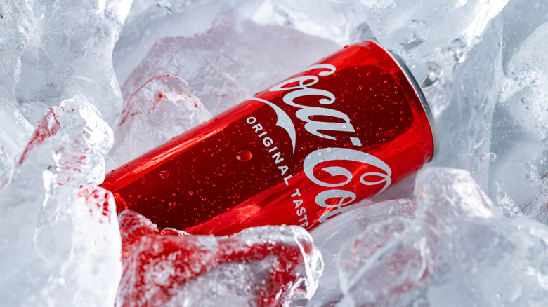 Red can of Coca-Cola soda nestled in pile of ice chunks
