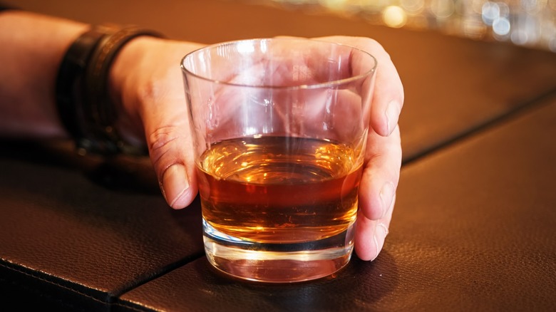 Hand holding neat bourbon in glass