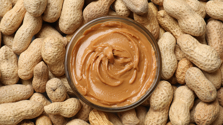 Overhead view of peanut butter in a bowl surrounded by ground nuts in shells
