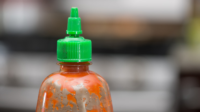 Closeup of the top of an empty sriracha bottle against a blurry background