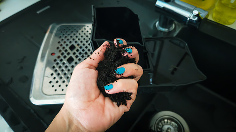 Hand holds spent coffee grounds above coffee machine