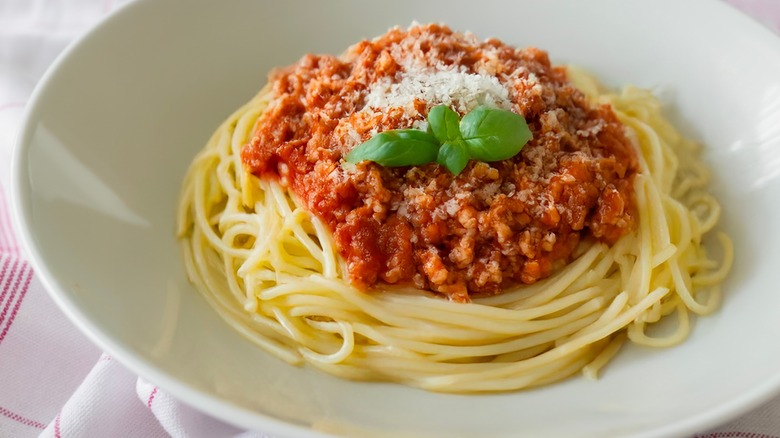 a meaty red bolognese sauce on top of spaghetti in a white bowl