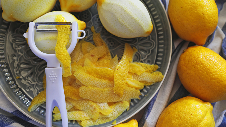 lemon peels, peeler, and whole lemons on a patterned plate