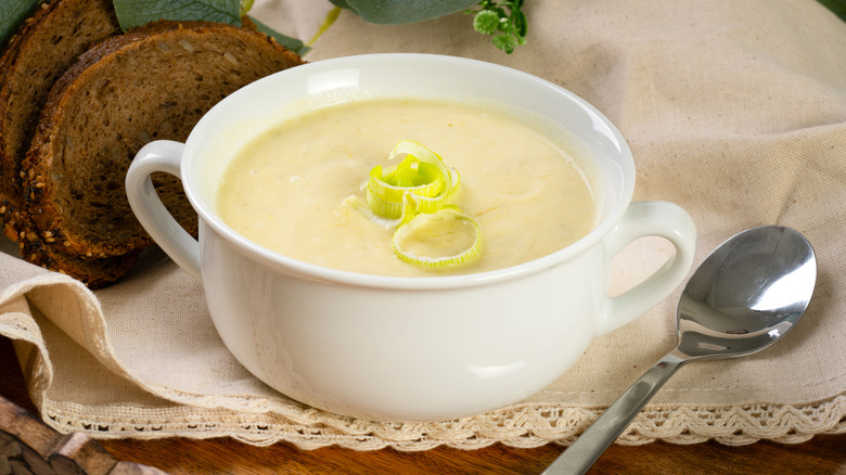 Bowl of creamy potato and leek soup on napkin with spoon and brown bread