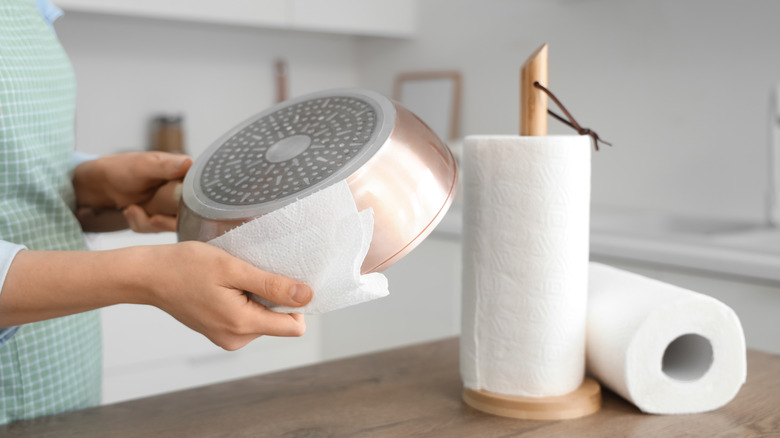A person wipes the bottom of a clean pan with a paper towel