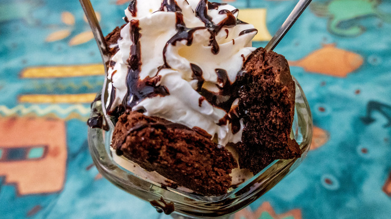 a brownie sunday in a glass bowl topped with whipped cream and chocolate sauce