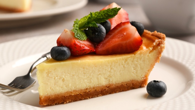 Slice of cheesecake topped with strawberries, blueberries, and mint leaves on white plate