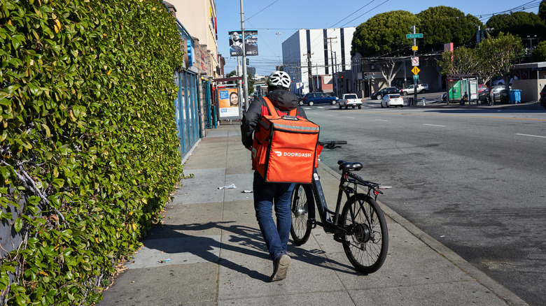 DoorDash delivery worker walking their bike along the sidewalk