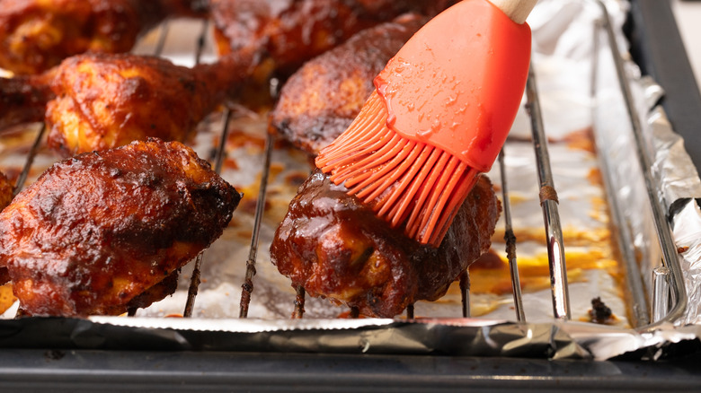 chicken getting brushed with barbecue sauce while on wire rack