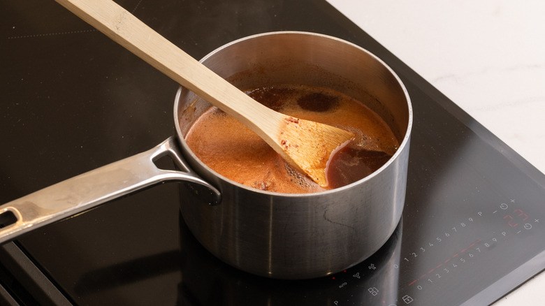 Dr Pepper barbecue sauce simmering in pot on stove with wooden spoon in pot