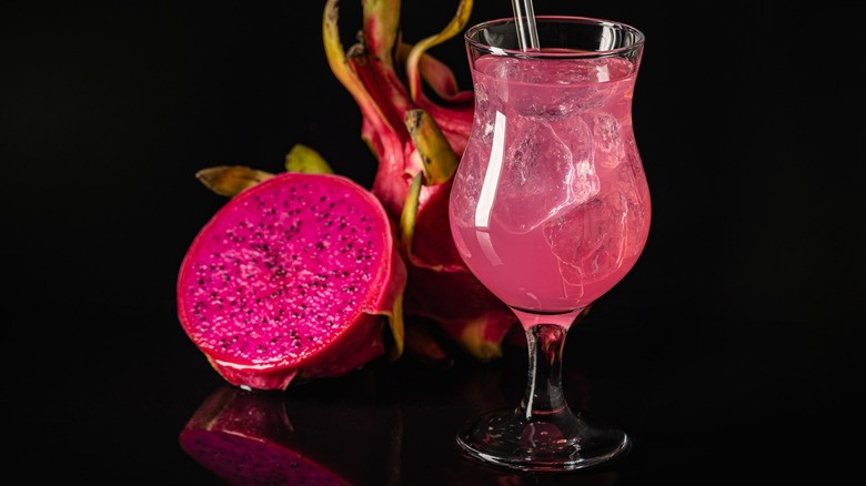 A pink cocktail next to dragon fruit on a dark background