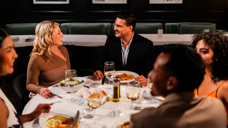 A group of friends sitting around a circular table eating dinner and drinking glasses of wine