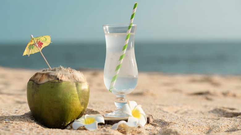 coconut water in a glass next to a coconut with a cocktail umbrella in it