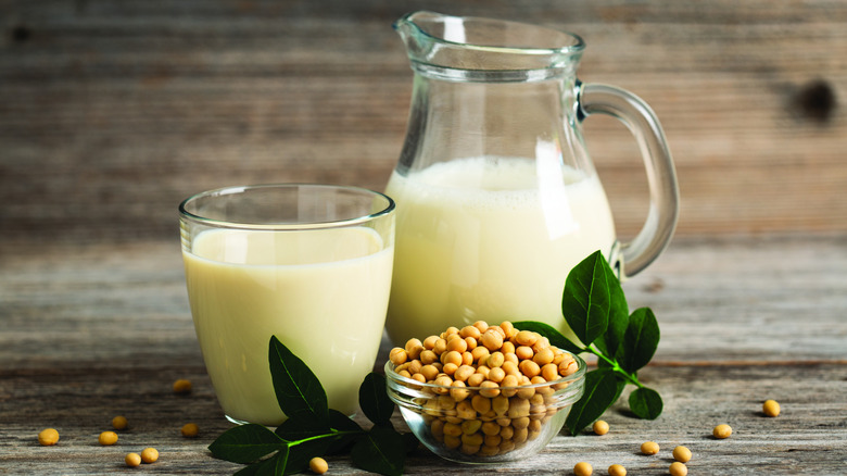 Soy milk in a glass and a jug alongside a bowl of soybeans