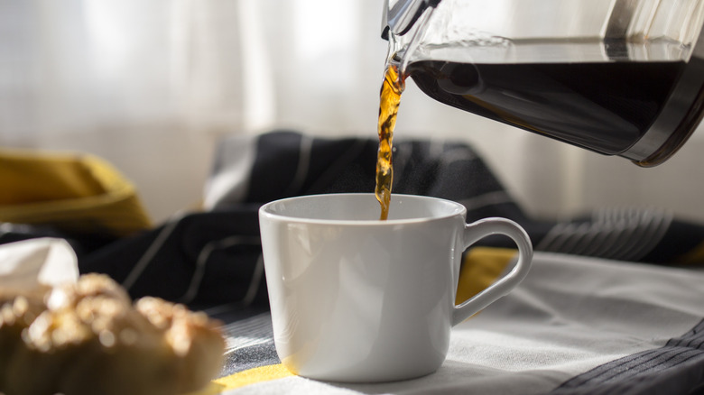 pouring filter coffee into a white mug from glass coffee pot