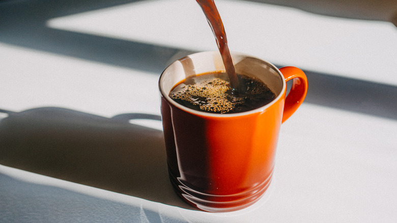 Orange mug of hot coffee being filled