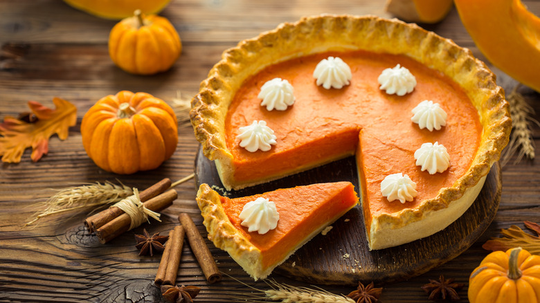 A pumpkin pie surrounded by small pumpkins and cinnamon sticks