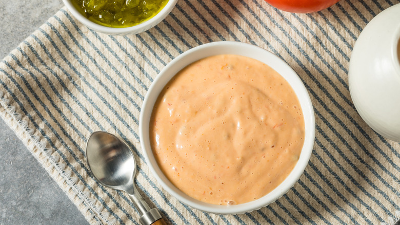 Bowl of Russian dressing on a table cloth with a spoon on the side