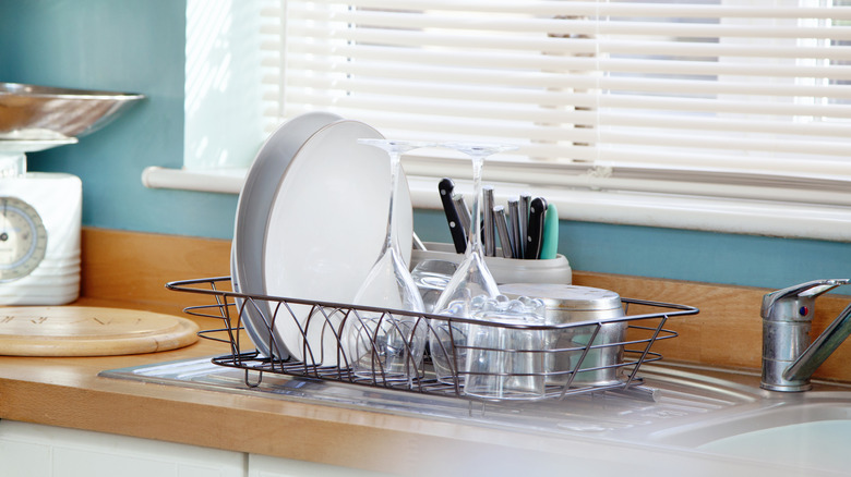 A drying rack featuring silverware, glasses, plates, and a pot next to a kitchen sink