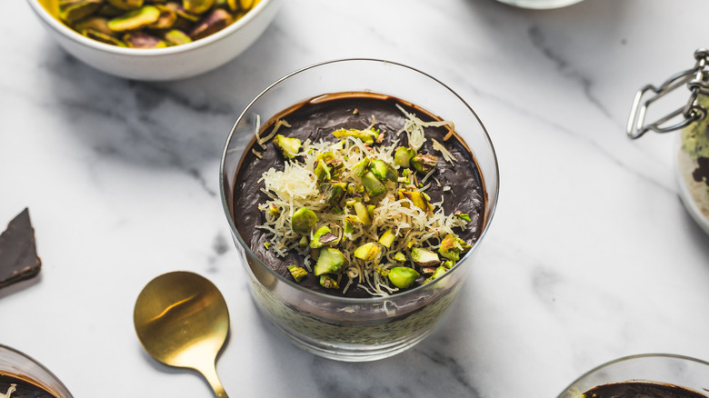 Close up on a cup of Dubai style pistachio chia pudding with spoon and more in background.